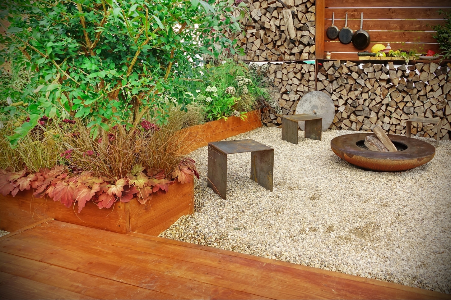Een buitenkeuken en vuurschaal in een tuin met siergrind.