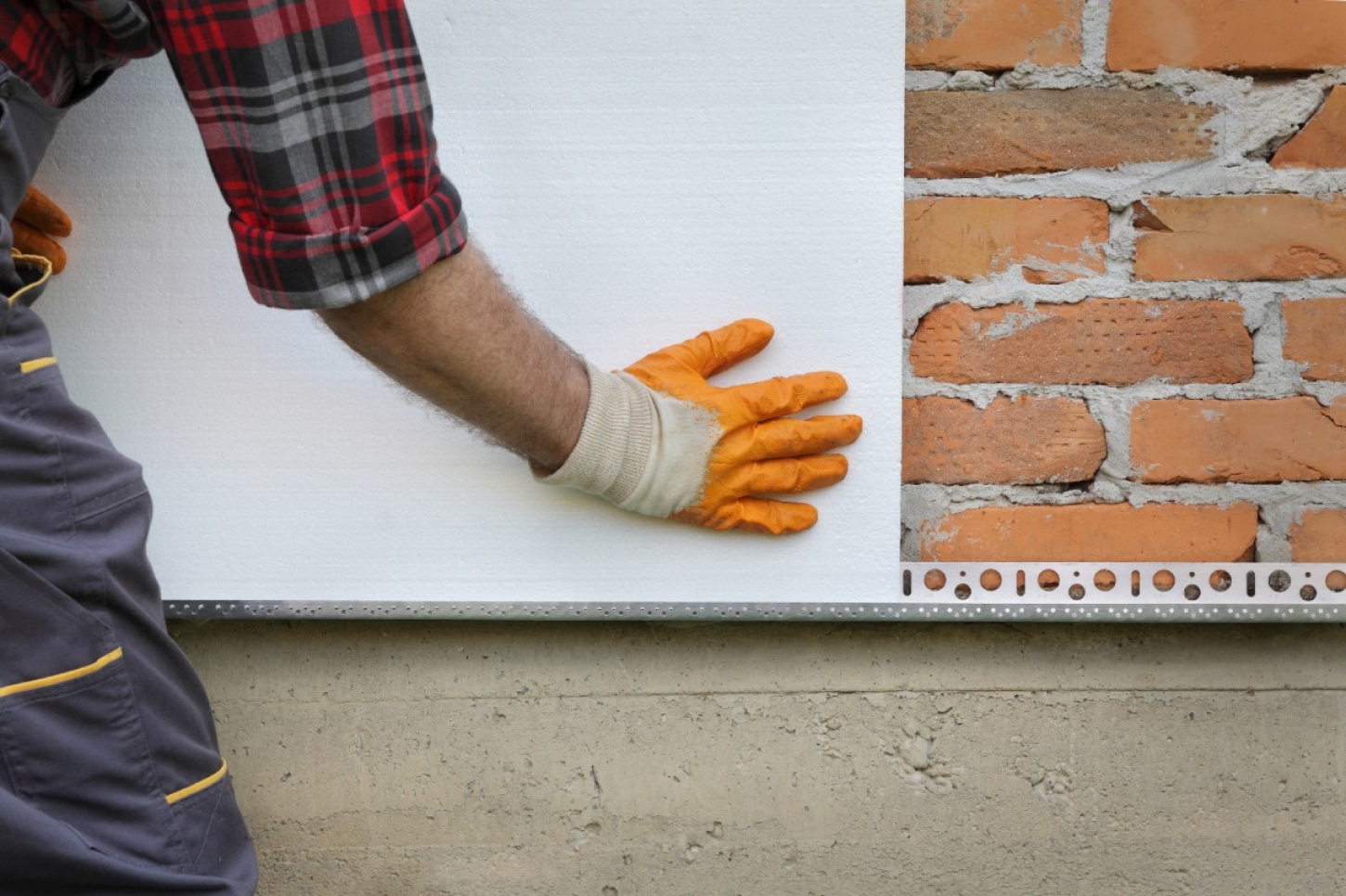Een werkman plaatst platen tegen de gevel van een woning.