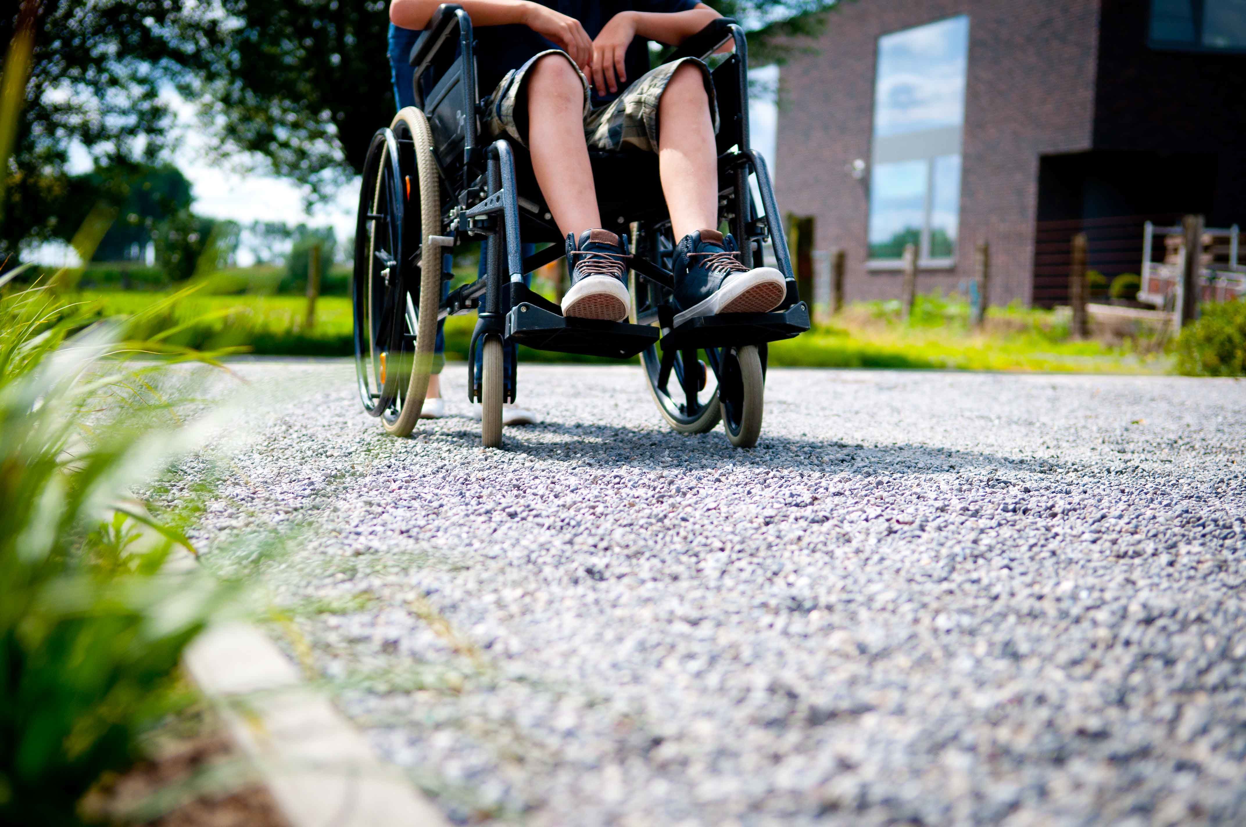 Man in rolstoel op grindpad.